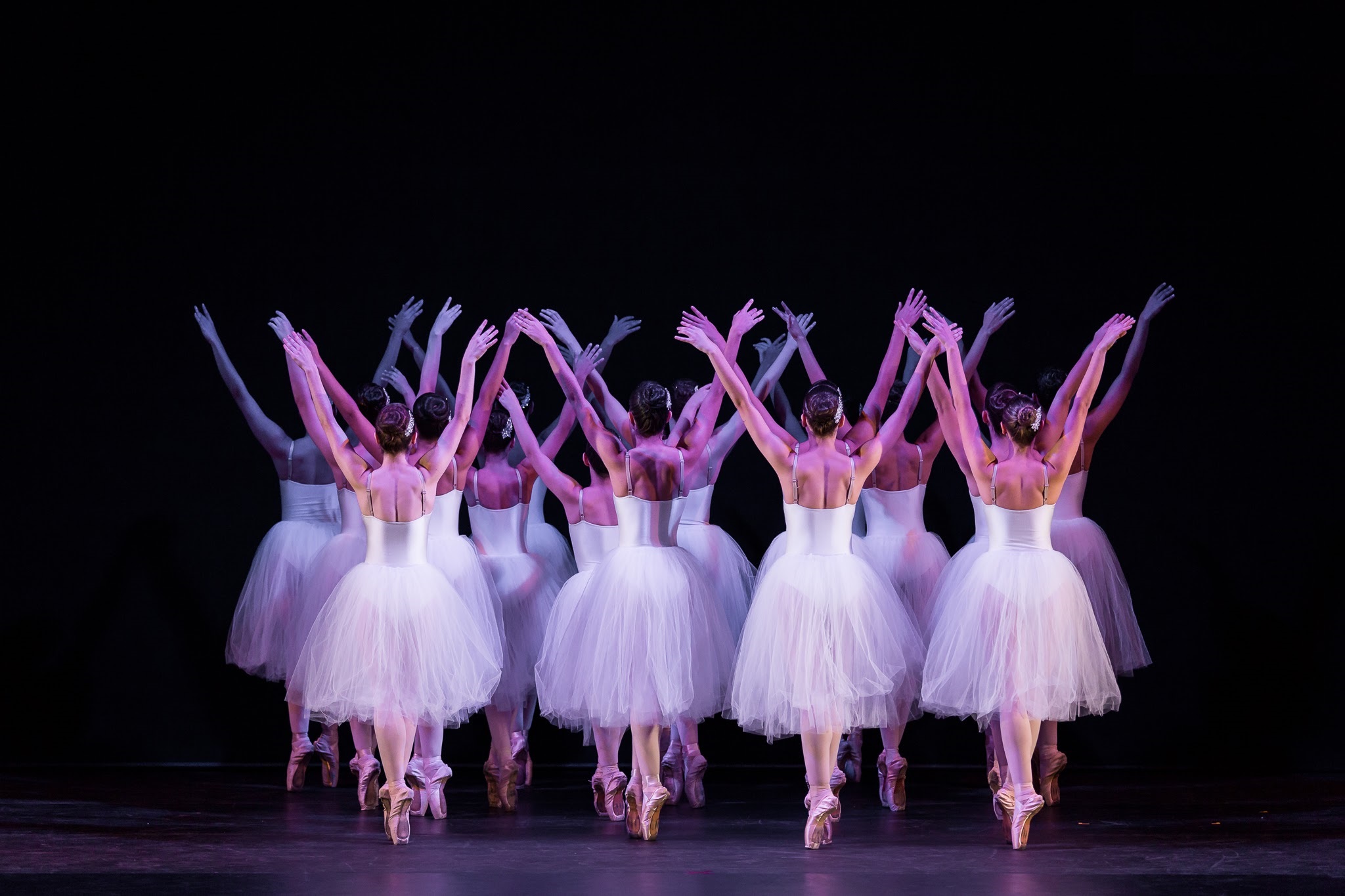 Bailarinas vestidas de branco se apresentando em um cenário escuro, com fundo preto.
