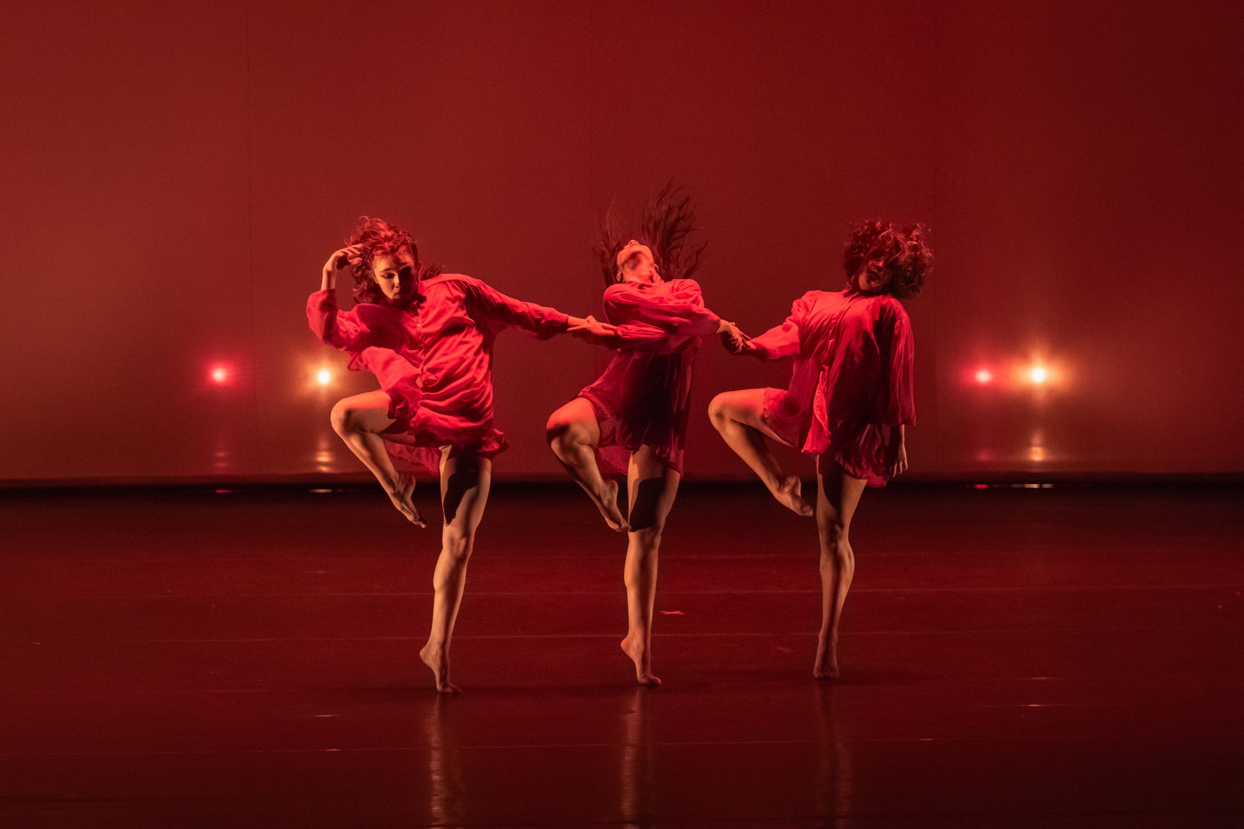 Foto de 3 bailarinas com roupas e luzes vermelhas dançando durante uma apresentação