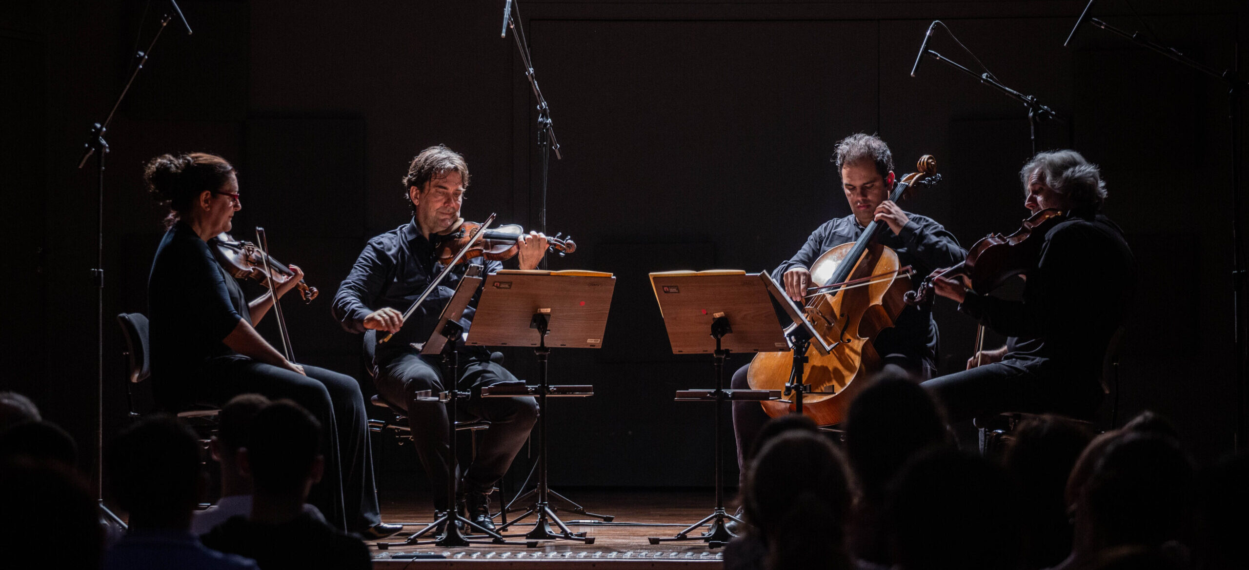 Os quatro membros do Quarteto de Cordas da Cidade de São Paulo sentados em círculo tocando seus respectivos instrumentos.