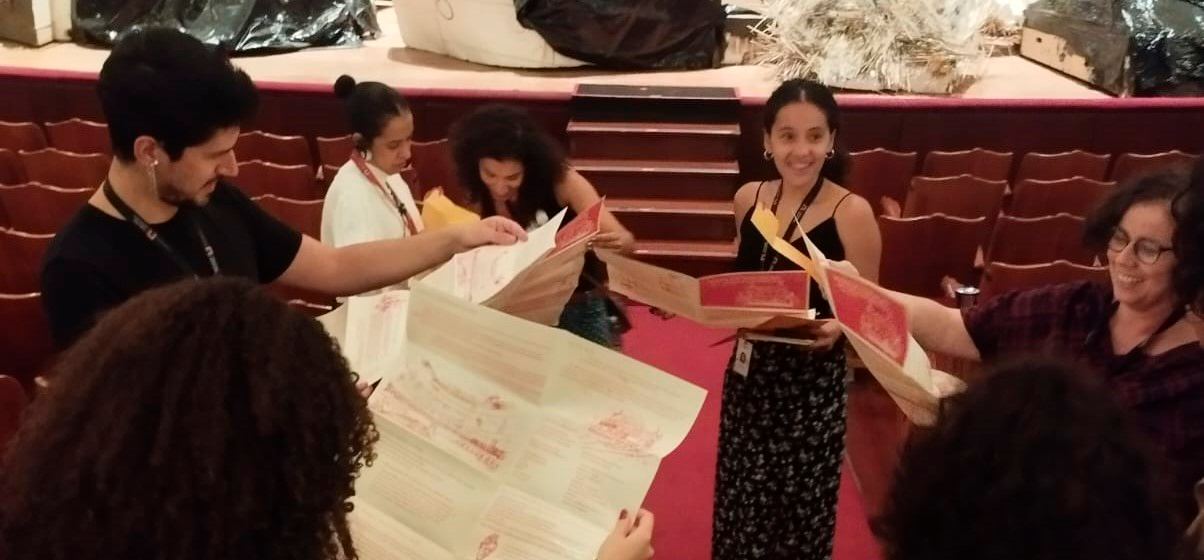 Pessoas em círculo lendo um panfleto sobre o núcleo de educação.